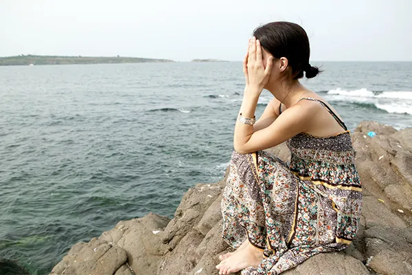 Woman sitting alone by the ocean with head in hands
