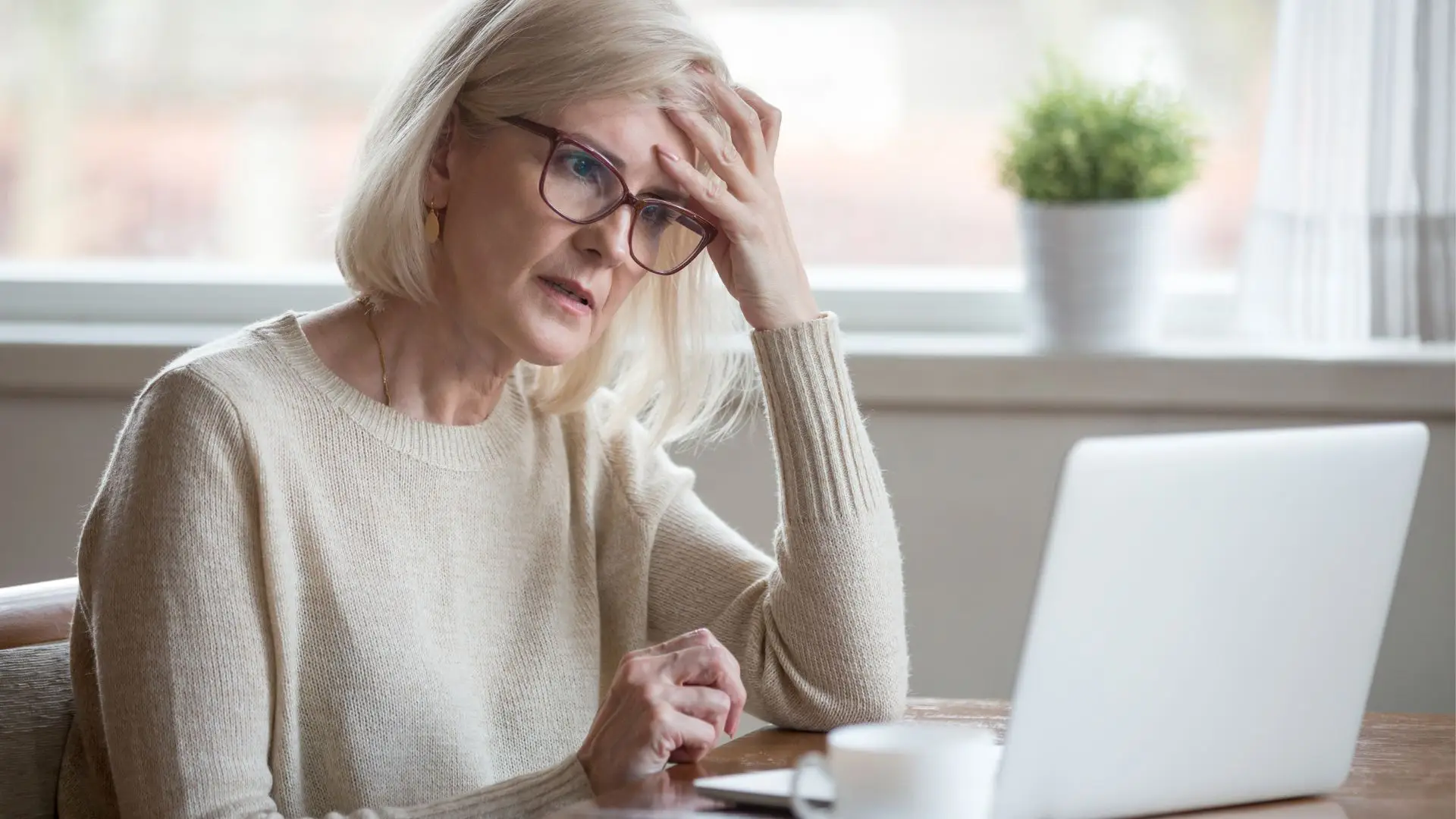 Older woman with glasses looking concerned at her laptop